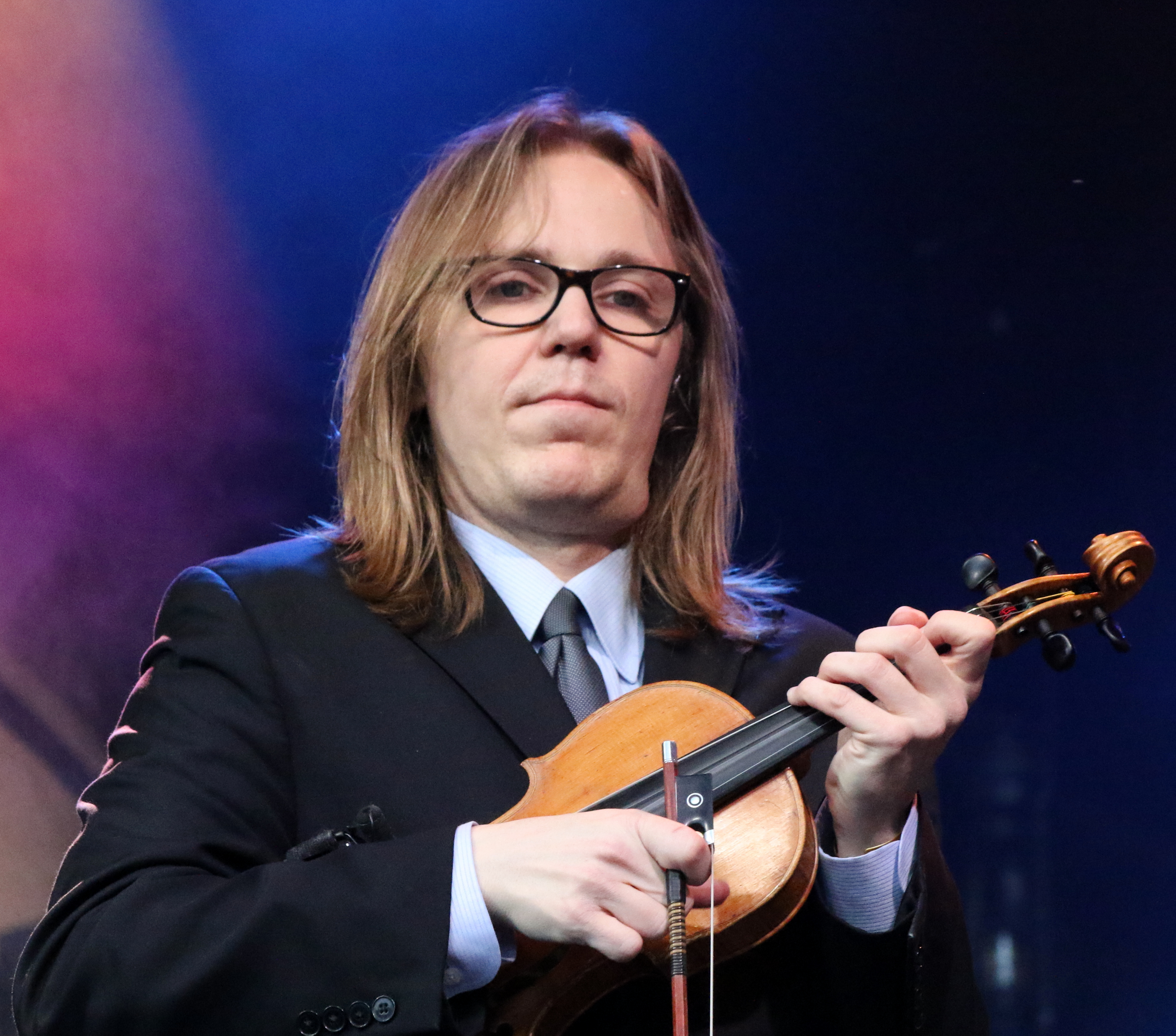 Bluegrass fiddler performing onstage at a festival with an audience behind the music